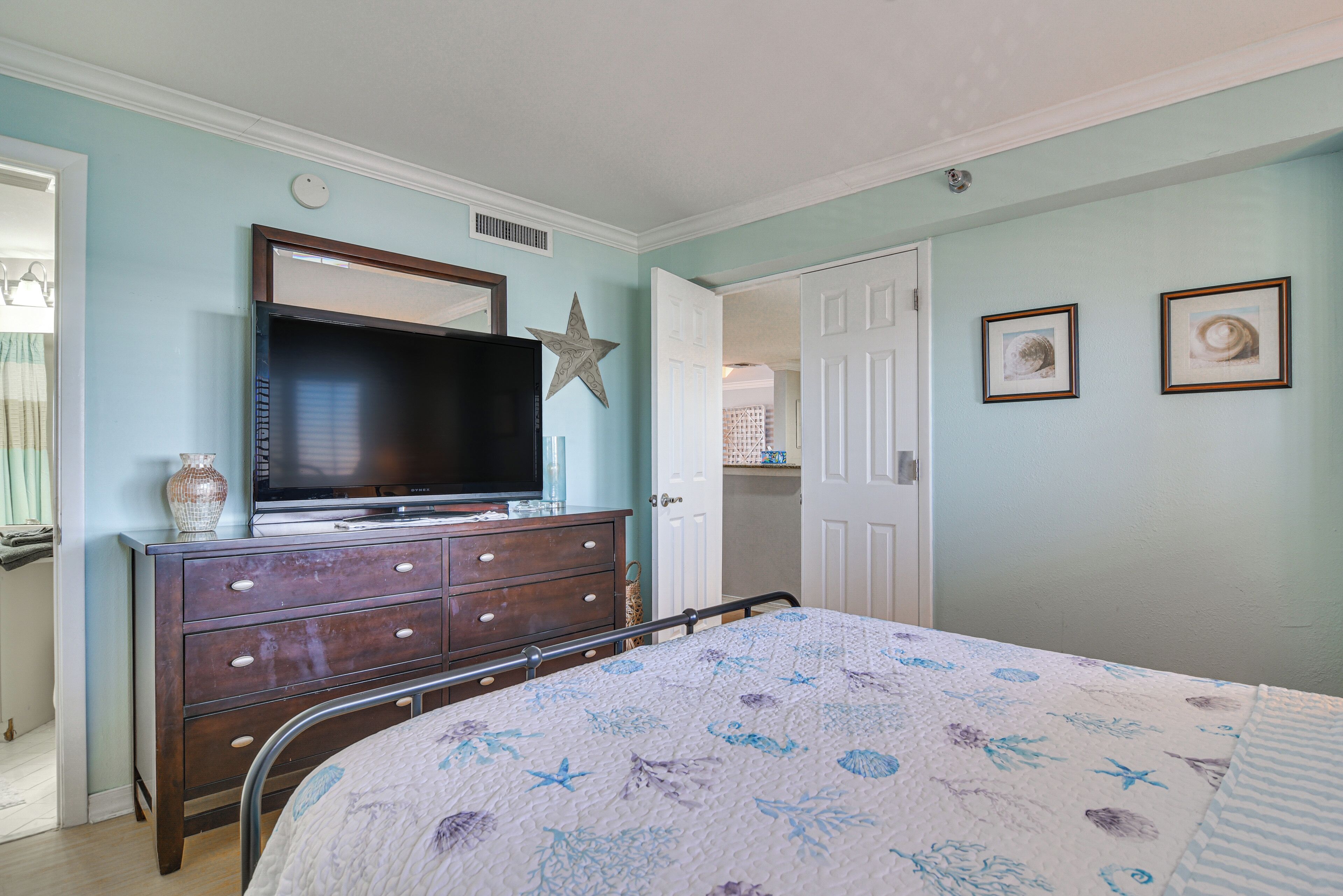 A bedroom with a bed, dresser, television, and two framed pictures on the wall.