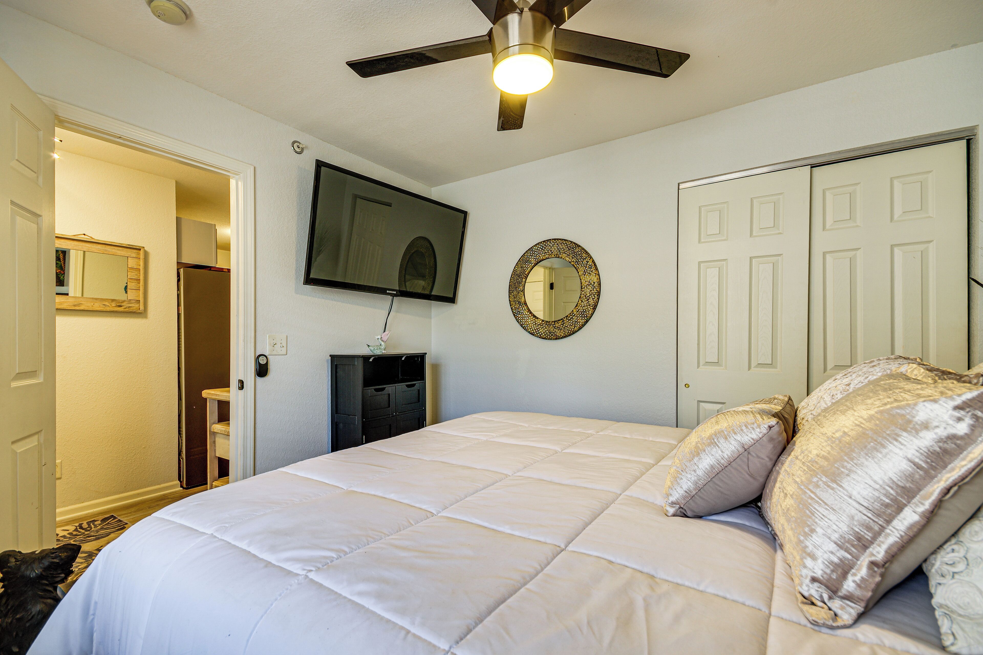 Un dormitorio con cama, ventilador de techo, televisión, espejo y puerta.