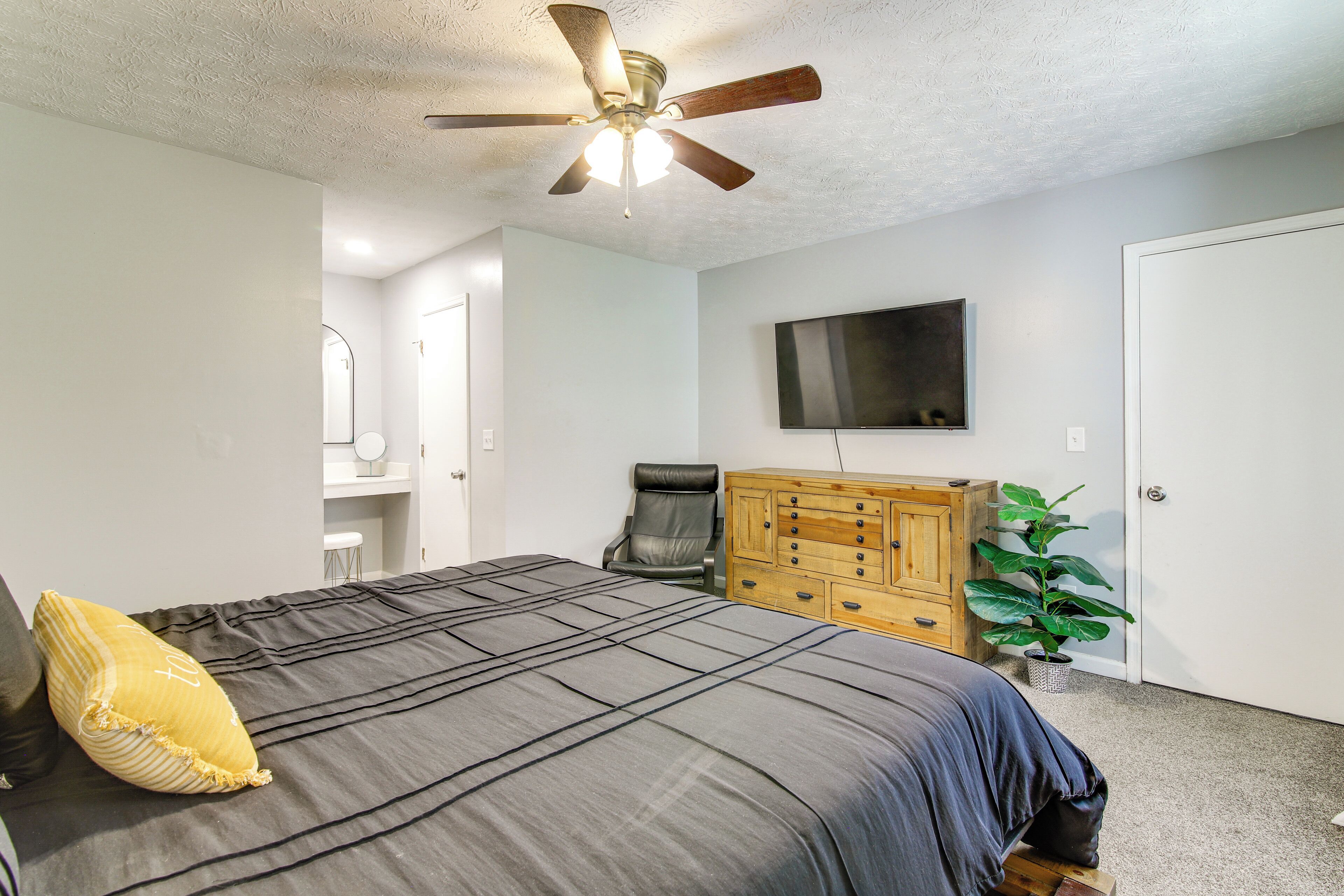 A bedroom with a bed, a ceiling fan, a dresser, a television, and a door.