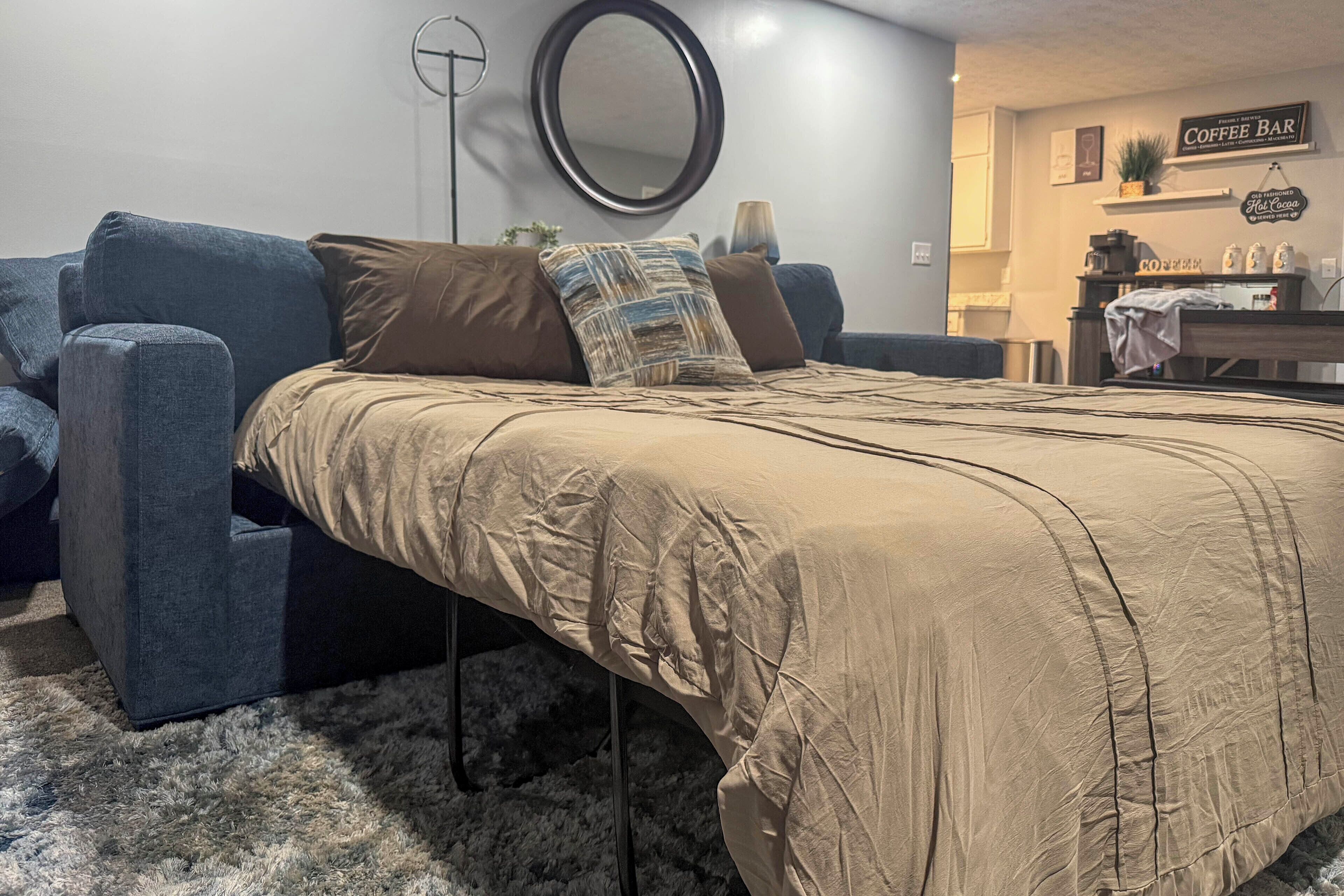 Ein Schlafzimmer mit einem Bett, einem blauen Sofa, einem runden Spiegel und einer Kaffeebar.
