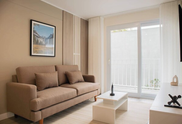 A modern living room with a beige sofa, a coffee table, and a large window with curtains. - w Stylish 1BR Apartment w Pool in Barranco (Lima)
