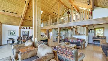 A spacious living area with high ceilings and wooden beams, featuring leather sofas, a dining area, and a staircase to an upper level.