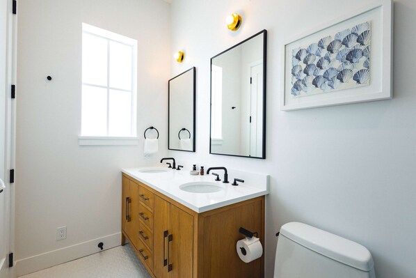 A bathroom with a white sink, wooden vanity, two mirrors, a framed artwork, and a toilet. - New Waterfront Home - Dreamside House (Key West)
