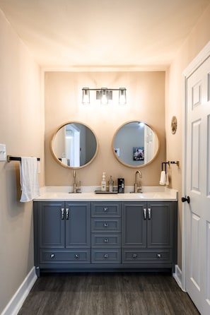 A bathroom with a double vanity, two round mirrors, a sink, and a towel rack.