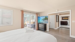 Ein geräumiges Schlafzimmer mit einem großen Bett, einem Fernseher und Blick auf einen tropischen Strand durch das Fenster.