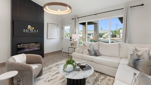 A modern living room with a fireplace, a sofa, a coffee table with decorative items, and a view of the outside. - NEW The Hensley on Hubbell Designer Oasis w Pool (Scottsdale)