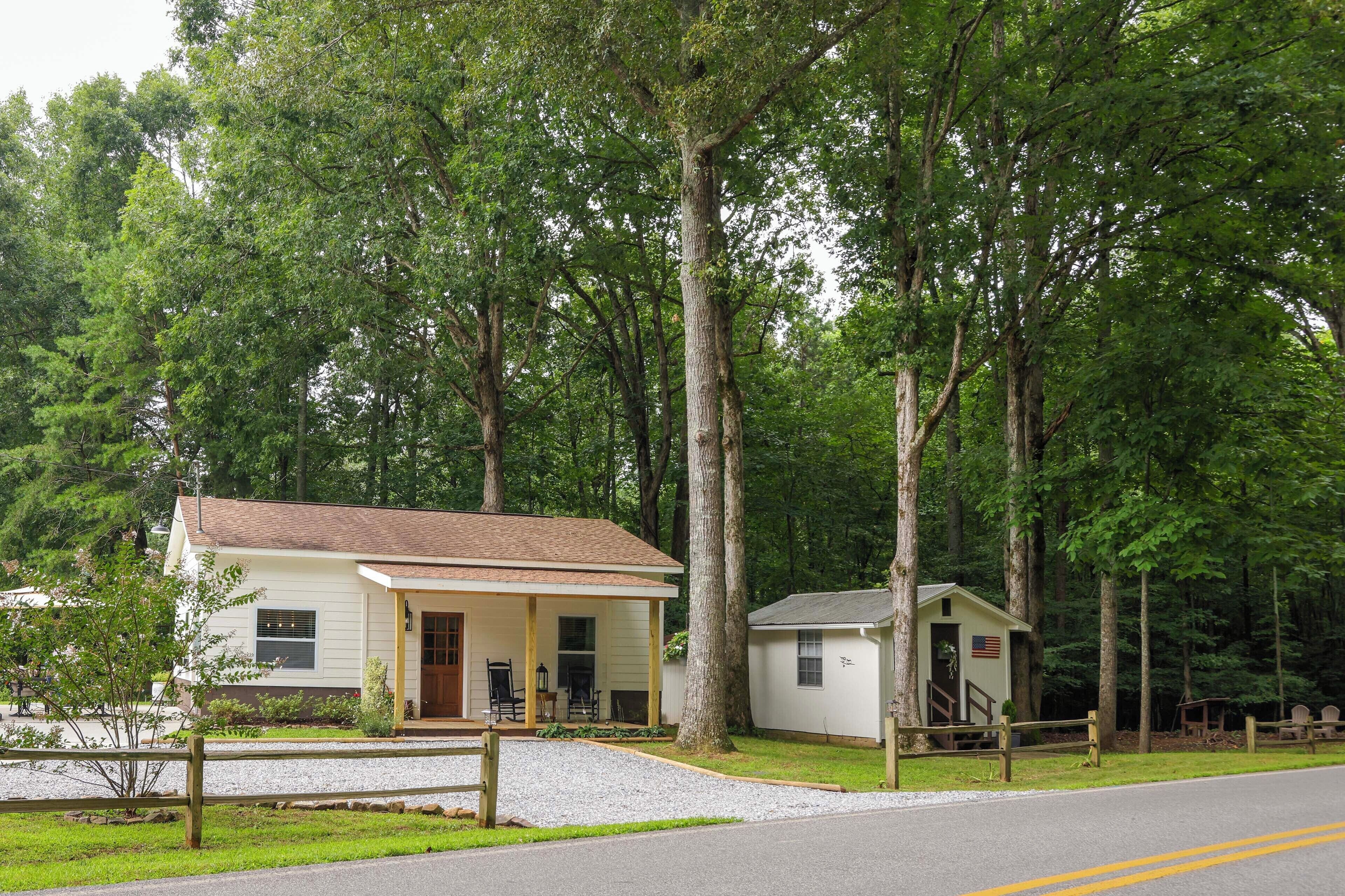 A small, single-story building with a porch and a small attached shed, surrounded by trees.