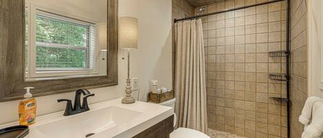 A bathroom with a large mirror, a sink, a toilet, and a shower area.