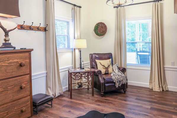 A room with a wooden dresser, a leather armchair with a deer pillow, a small table with a lamp, and a wall-mounted coat rack. - 1/2 Mi to Lake Nottely: Blairsville Home w/ Patio! (Blairsville)