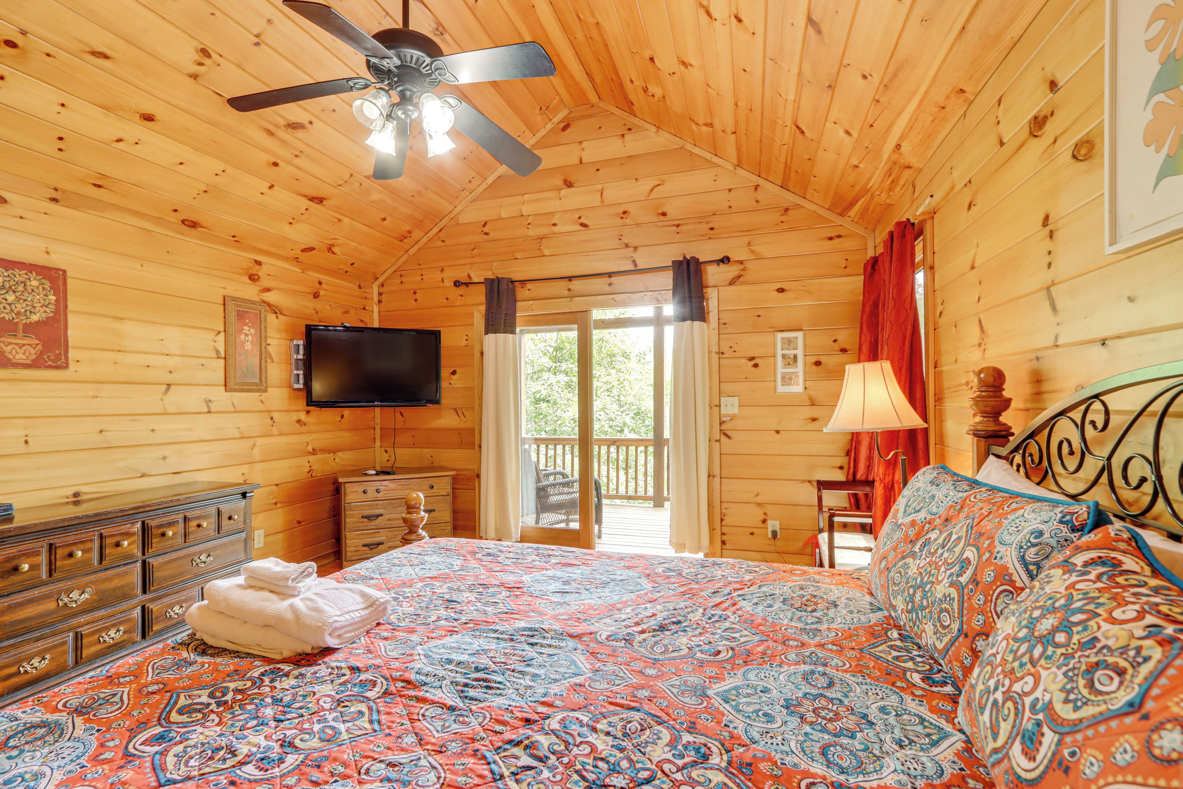 A wooden cabin bedroom with a bed, dresser, TV, and a balcony door.
