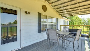 A covered outdoor patio with a table and chairs, a window with shutters, and a metal roof.