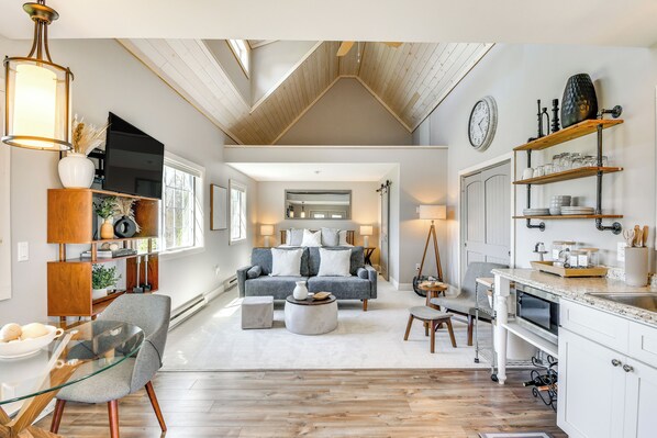 Amplia sala de estar con techo alto, un rincón de estar acogedor y una cocina con muebles blancos y encimera de madera.