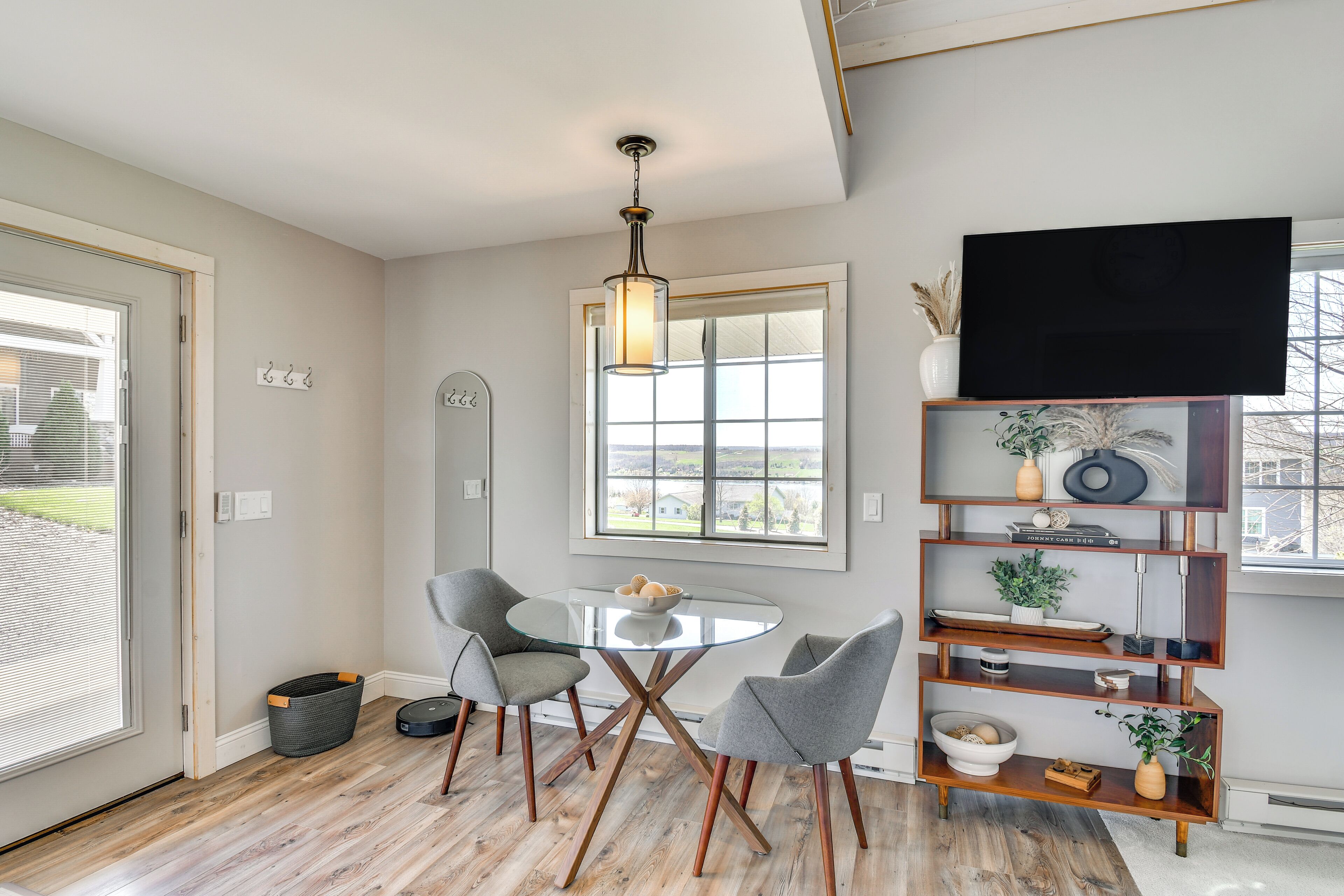 A modern dining area with a glass table, grey chairs, and a wooden floor.