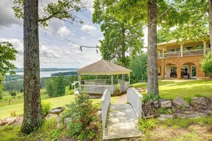 A gazebo with a stone pathway leading to a covered patio area, surrounded by lush greenery and a view of a lake. - 1 Mi to Lake Guntersville: Scenic Condo Retreat! (Grant)