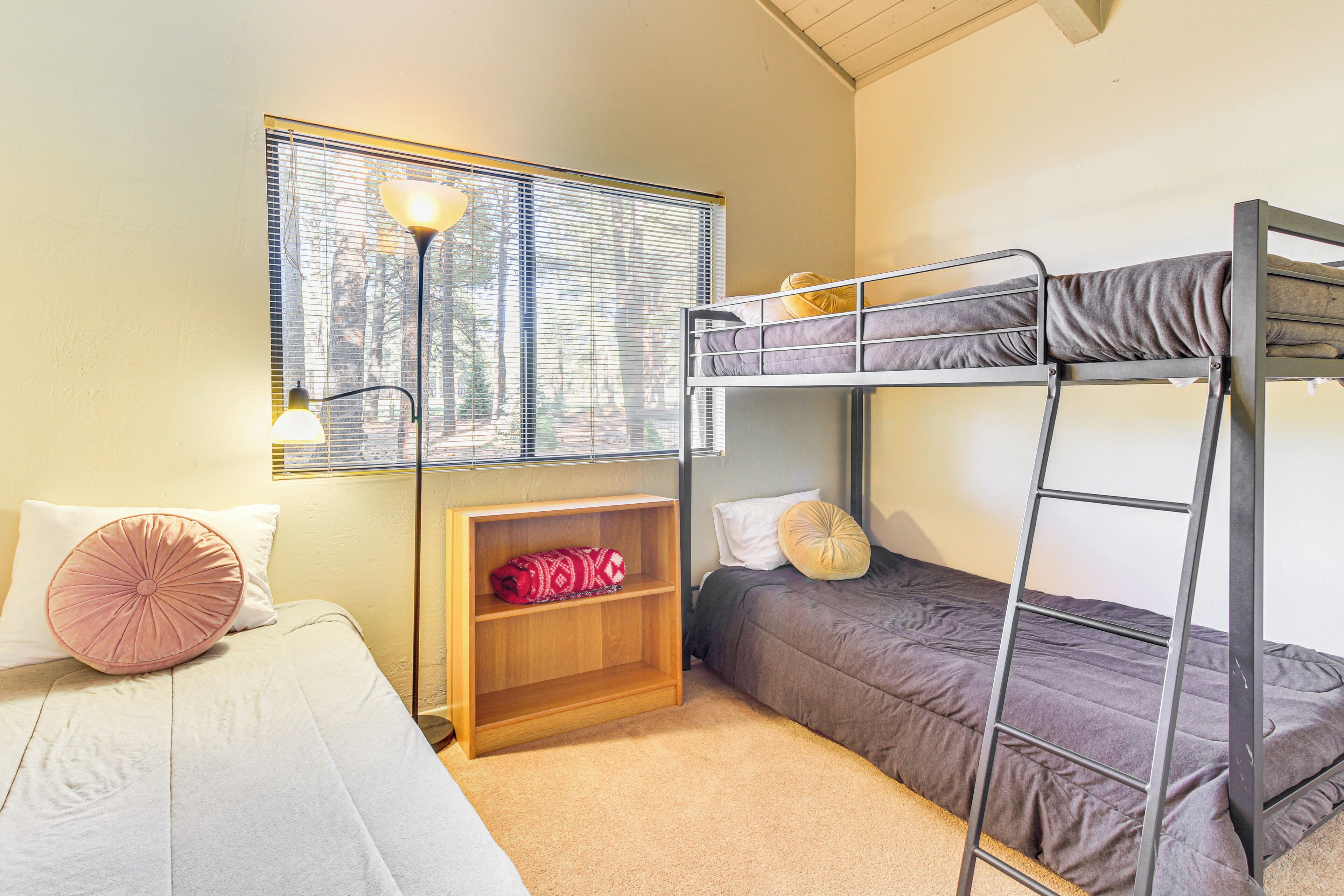 A bunk bed room with a window, a desk with a lamp, and a bookshelf.