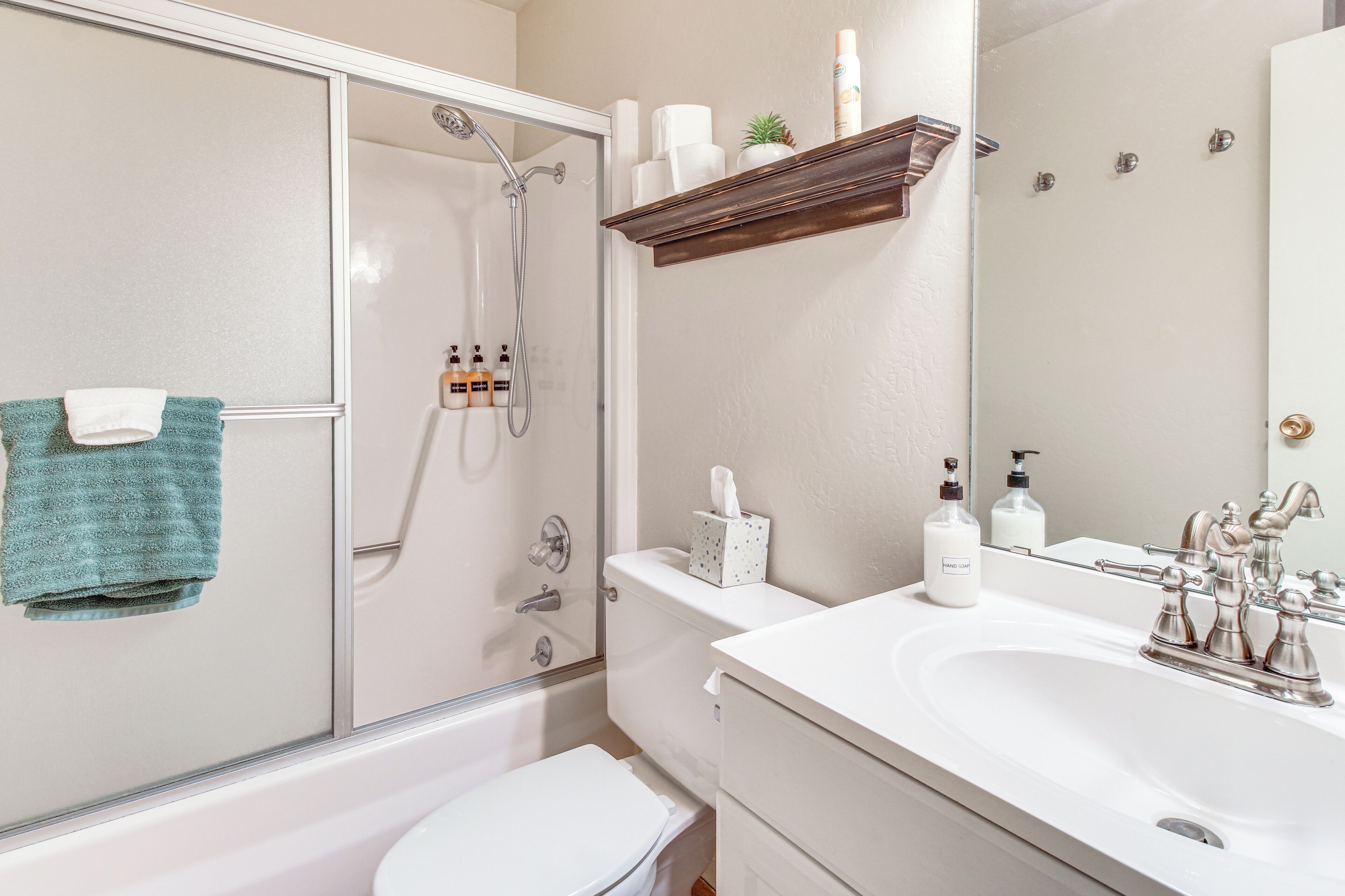 A bathroom with a glass shower enclosure, a white toilet, a sink with a mirror, and toiletries on the counter.