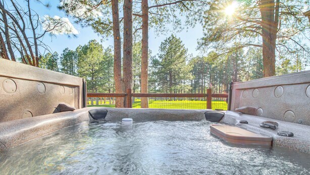 A hot tub with a wooden deck and a view of a grassy area and trees. - Golf Course Getaway & Hot Tub Haven in Pinetop! (Pinetop)