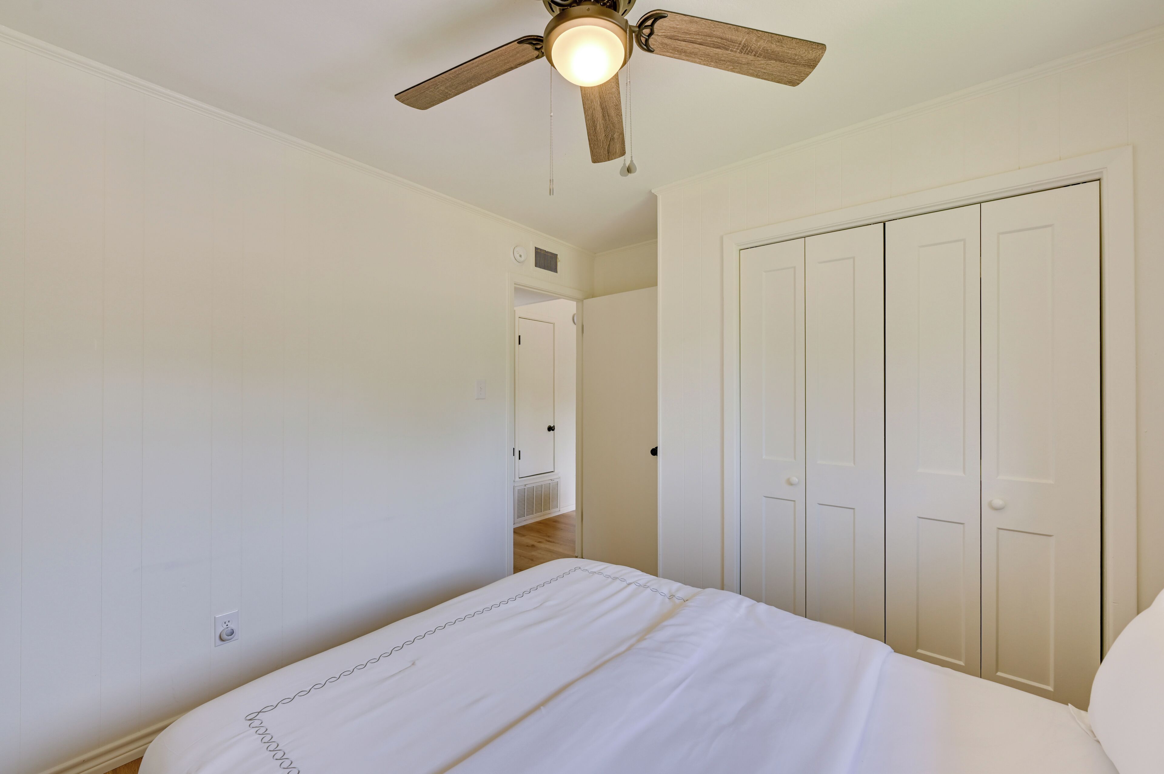 A bedroom with a bed, a ceiling fan, and a wardrobe.