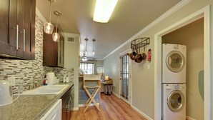 A kitchen with wooden cabinets, a granite countertop, a sink, and a dishwasher. There is a double oven and a washing machine in the adjacent room. - Walk to SFA Campus: Pet-friendly Nacogdoches Condo (Nacogdoches)