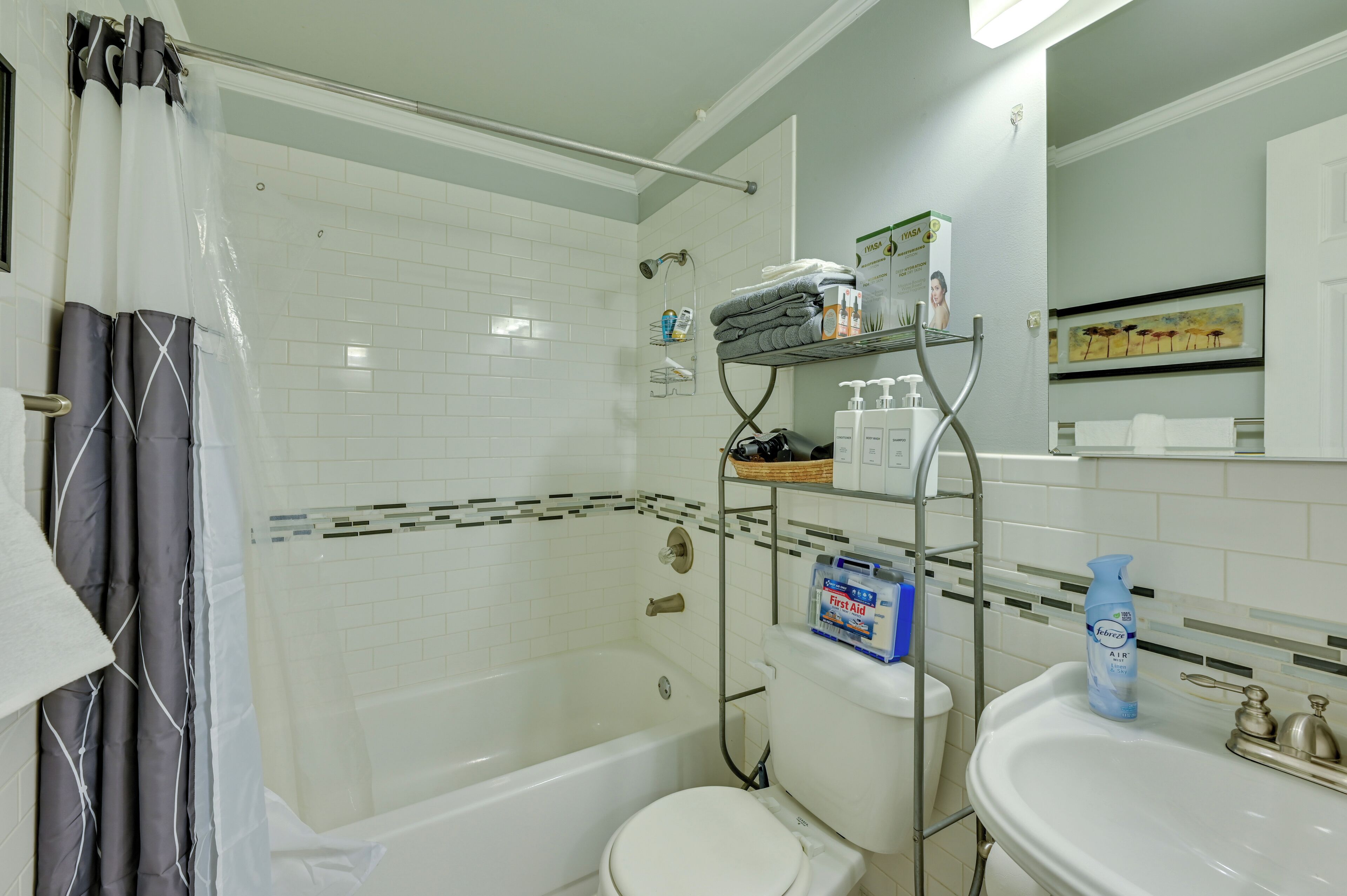 A bathroom with a bathtub, toilet, and sink. There are shelves with toiletries and a shower curtain.