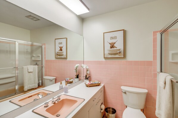 Ein Badezimmer mit einem Doppelwaschbecken, Toilette und Dusche. An der Wand befinden sich Bilder in Rahmen und ein Handtuchhalter.