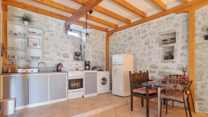 A kitchen with stone walls, wooden beams, a sink, cabinets, a stove, a washing machine, and a dining table with chairs. - Holiday Home 'Lainaki' with Sea View, Wi-Fi and Air Conditioning (Lefkada)