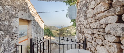 A stone-walled courtyard with a round table and chairs, a metal gate, and a hanging lantern.