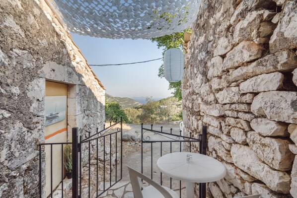 A stone-walled courtyard with a round table and chairs, a metal gate, and a hanging lantern.