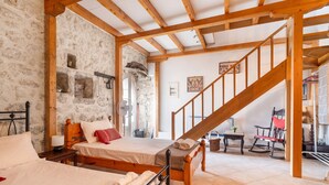 A bedroom with a wooden bed, a wooden staircase, stone walls, and a small table with a chair. - Holiday Home 'Lainaki' with Sea View, Wi-Fi and Air Conditioning (Lefkada)
