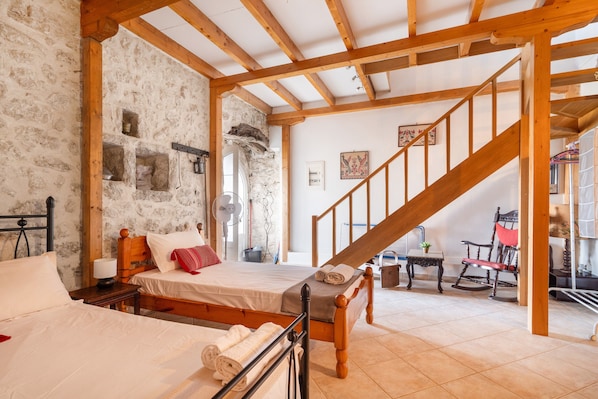 A bedroom with a wooden bed, a wooden staircase, stone walls, and a small table with a chair.