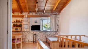 A room with a stone wall, wooden ceiling, a TV, a window, a wooden bench, and a table with chairs. - Holiday Home 'Lainaki' with Sea View, Wi-Fi and Air Conditioning (Lefkada)