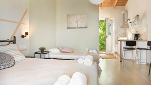Ein Schlafzimmer mit zwei Betten, einem kleinen Tisch mit Pflanze, einem Bild an der Wand und einer Küchenzeile mit Barhocker.