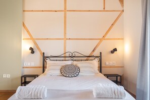 Een net opgemaakt bed met een decoratief kussen, twee nachtkastjes en een houten balkenplafond.