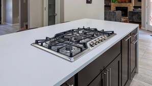 A modern kitchen with a central island, dark cabinetry, and a built-in gas stove. - 4 Bed, 3.5 Bath Home with Heated Pool (El Paso)