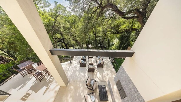 Un patio moderno al aire libre con una zona de estar, una chimenea y vistas a un jardín exuberante.