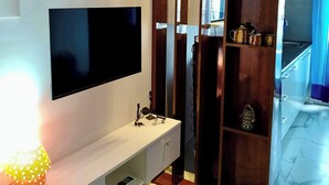 Uma sala de estar moderna com uma televisão de tela plana na parede, uma mesa de console branca com abajur e um armário de madeira com prateleiras.