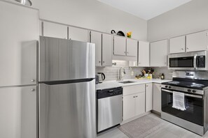 A modern kitchen with stainless steel appliances, white cabinetry, and a tiled backsplash.