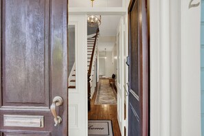 A wooden door with a brass handle, a white wall, and a staircase leading to an upper floor. - Steps from Forsyth Park-Parking Spot Included! (Savannah)