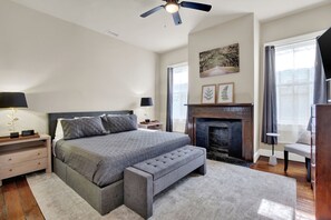 Ein Schlafzimmer mit einem Bett, Nachttischen, einer Bank, einem Kamin und einem Deckenventilator.