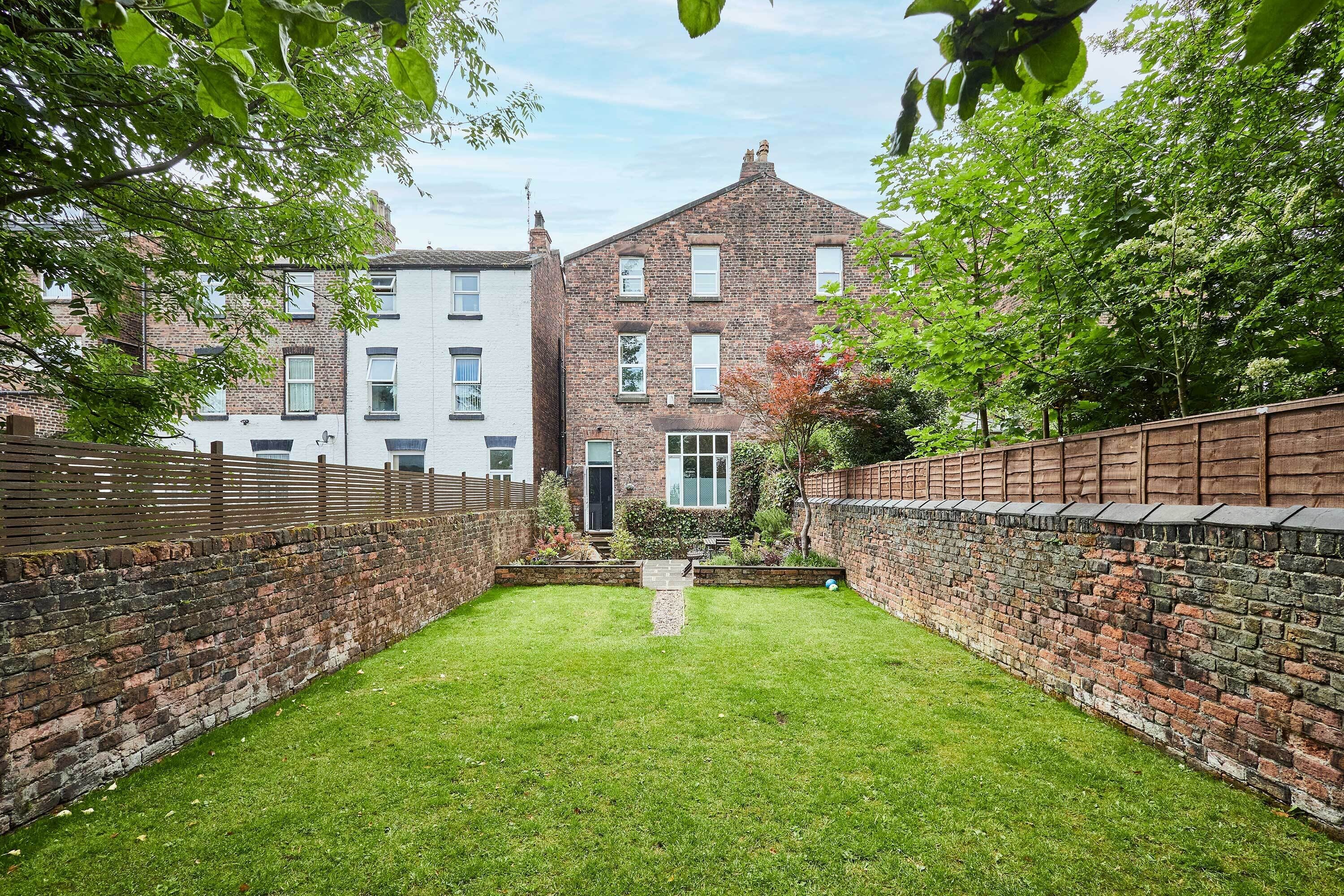 A courtyard with a brick wall, a grassy lawn, and a building with multiple windows and a door.