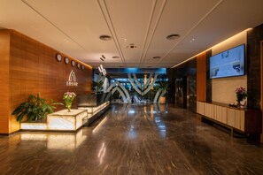 A modern hotel lobby with a marble floor, wooden paneling, a reception desk, and a large digital display. - Arcor Hotels Mysuru (Mysore)