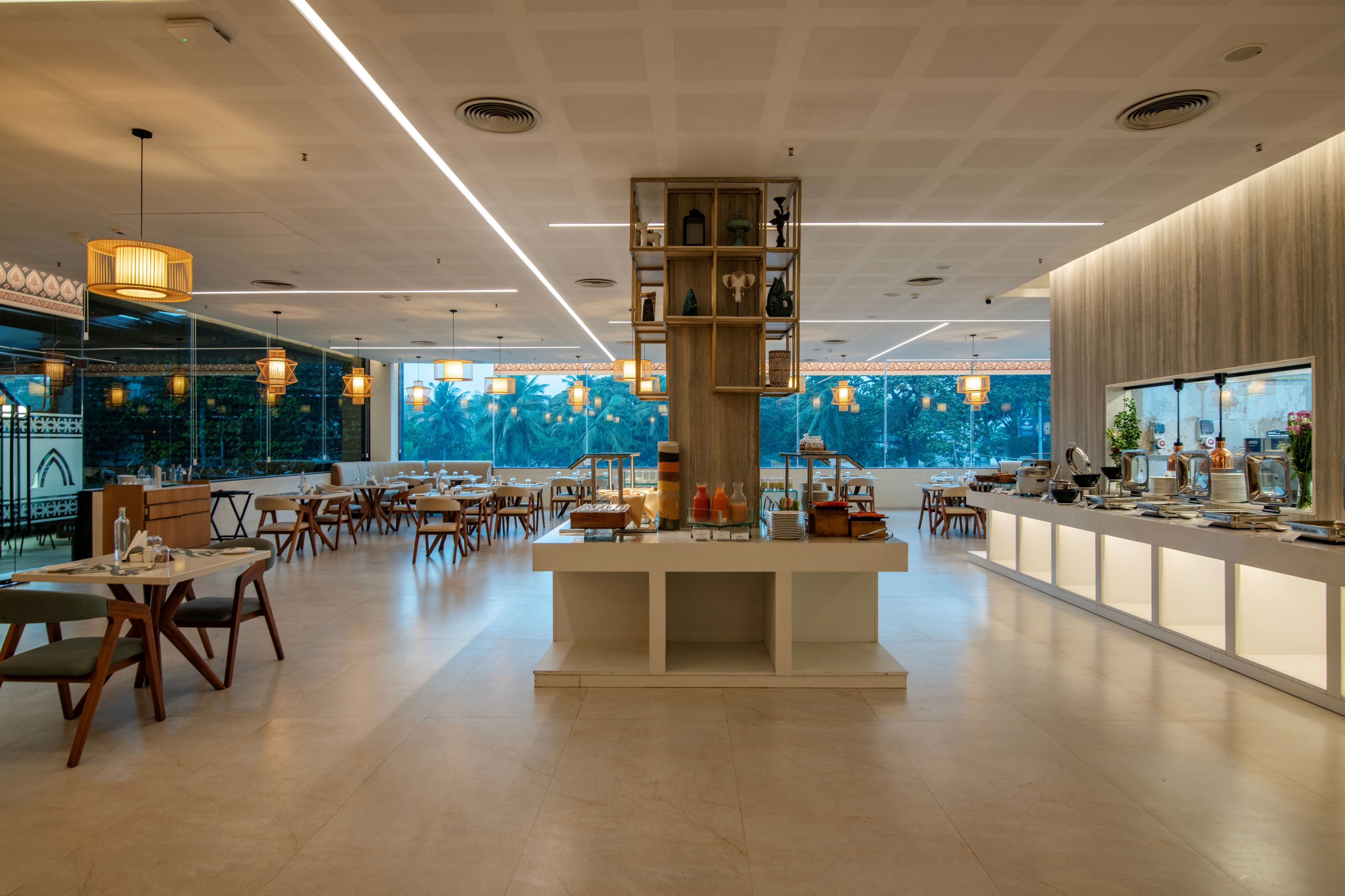 A spacious restaurant with a central serving area, multiple seating arrangements, and large windows offering a view of the outdoors.