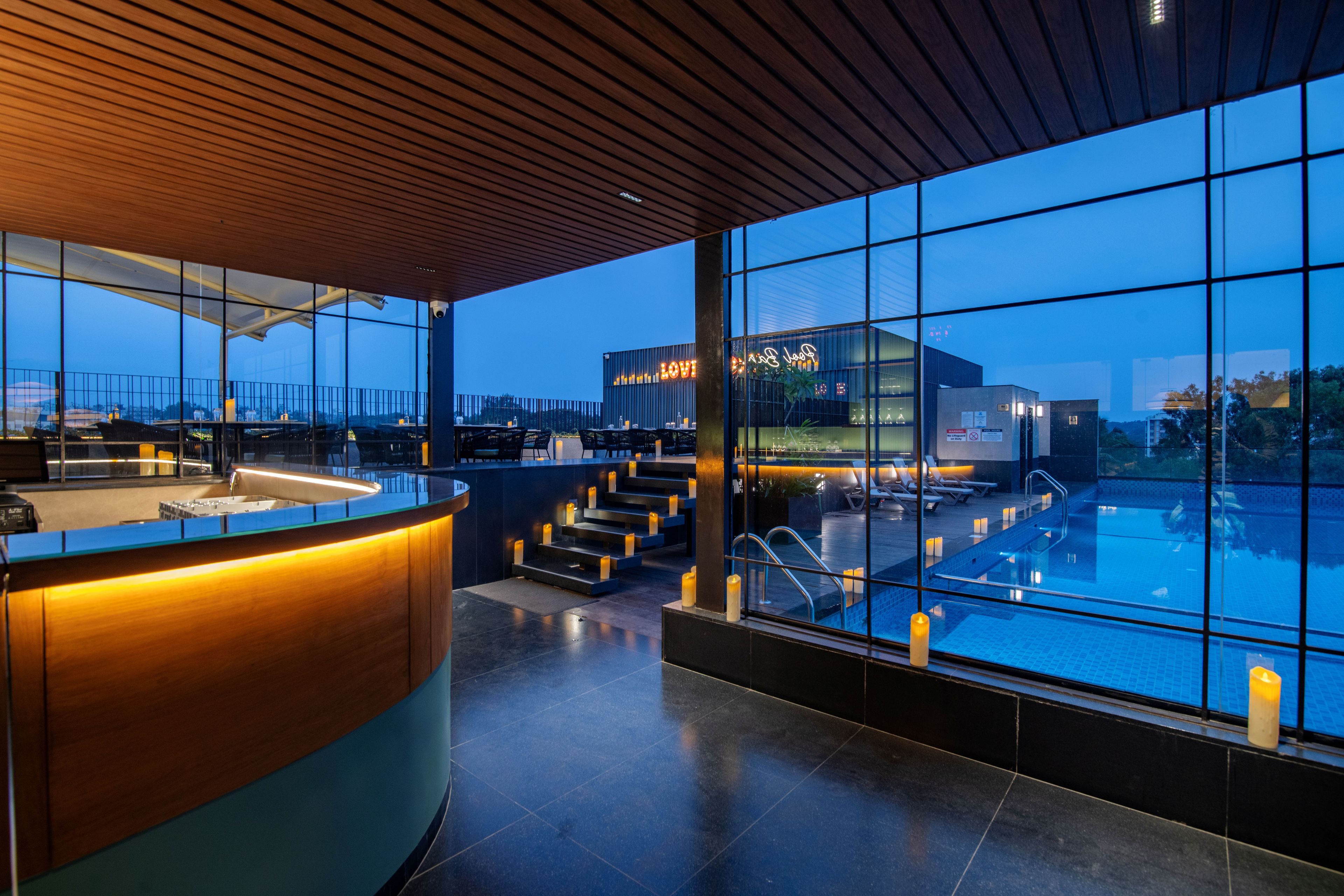 Un espace piscine intérieur moderne, doté d’un bar, d’un coin salon, de grandes fenêtres et offrant une vue sur le paysage urbain.