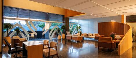 A modern lobby with a reception desk, seating area, and a staircase leading to upper floors.