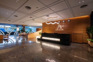 Zona de recepción de hotel con un mostrador de mármol, paneles de madera y un reloj de pared que muestra múltiples zonas horarias.