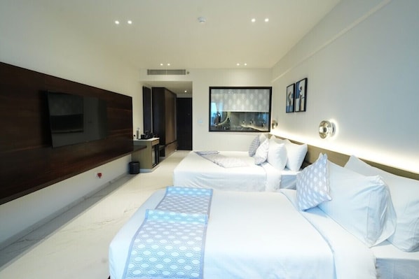 A modern hotel room with two beds, a TV, a large mirror, and a small bathroom.