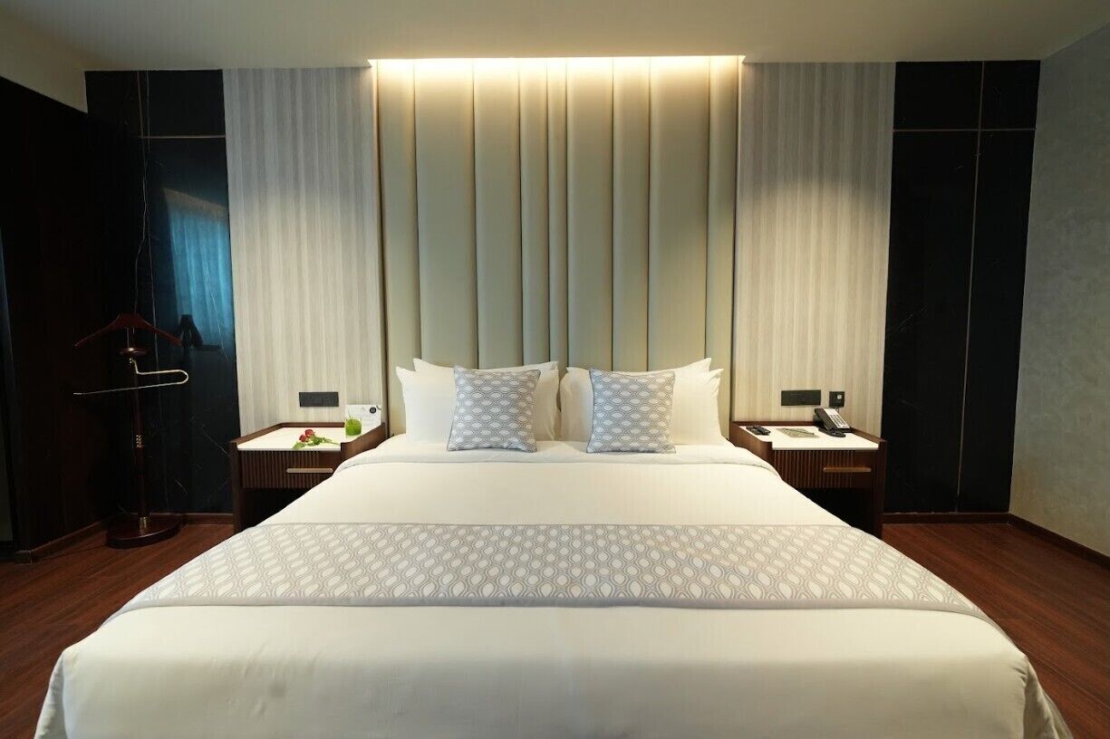 A hotel room with a large bed, two bedside tables, a wardrobe, and a curtain wall.