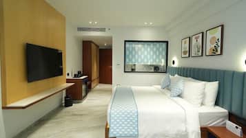 A hotel room with a bed, a TV, a desk, and a bathroom visible through a glass door.