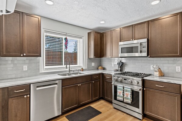 A modern kitchen with wooden cabinets, stainless steel appliances, and a window with blinds.