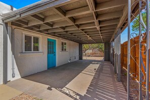A covered patio area with a concrete floor, a blue door, and a wooden fence.
